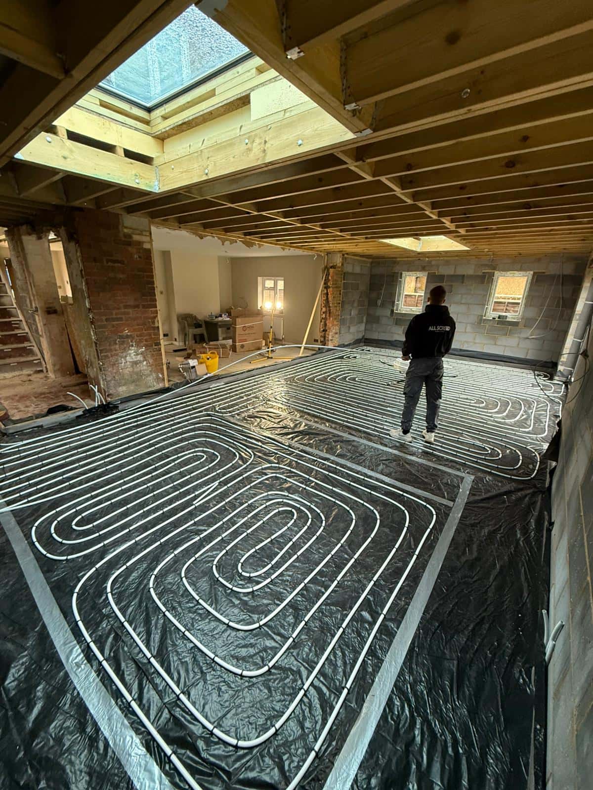 One of the crew, in an All Screed top, walking across underfloor heating pipe laid in a large extension at Tongham
