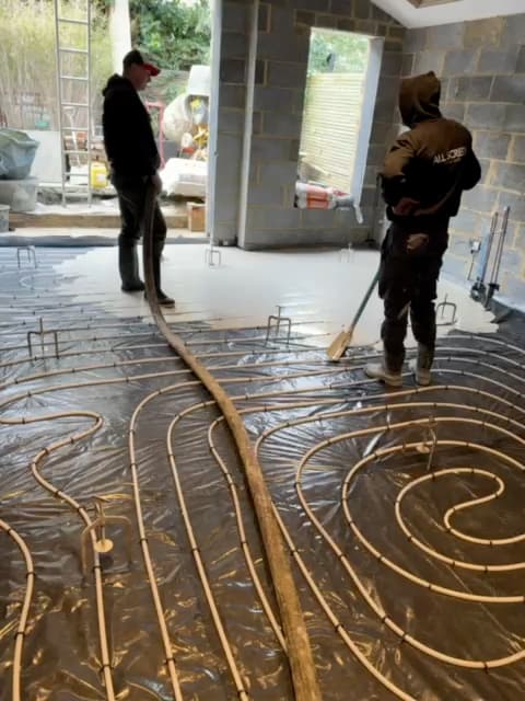 Two of the crew at the Brixton job, one holding the screed hose as the screed spreads over the underfloor heating pipe